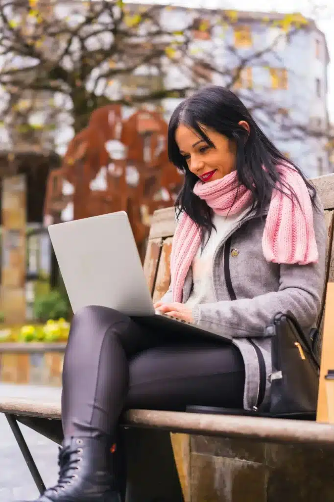 A Caucasian brunette girl reading a book in a city park, smiling sitting on a bench