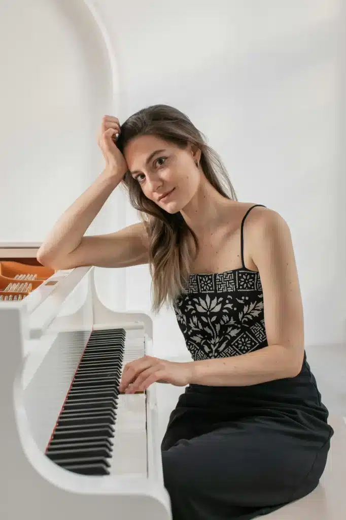 A young elegant female musician in a black dress by the grand piano, leaning on it with her elbow