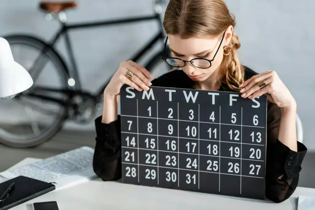 beautiful businesswoman in black clothes and glasses sitting on chair and looking at calendar