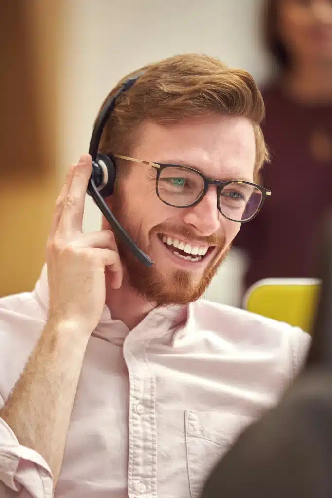 Businessman Wearing Headset Talking To Caller In Busy Customer Services Centre