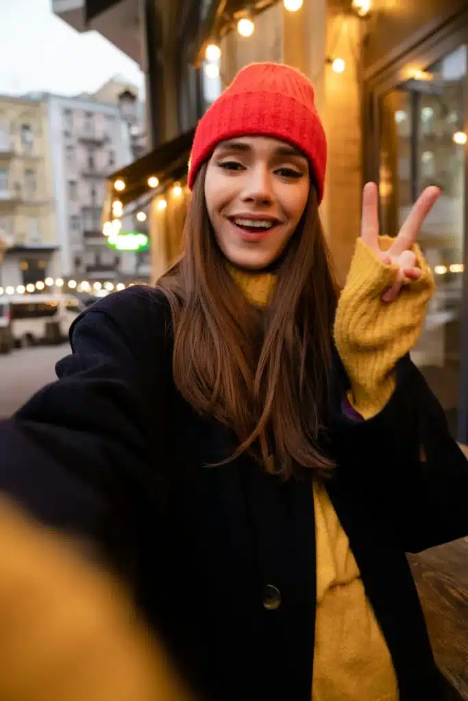 Charming happy girl gesturing peace sign while taking selfie photo