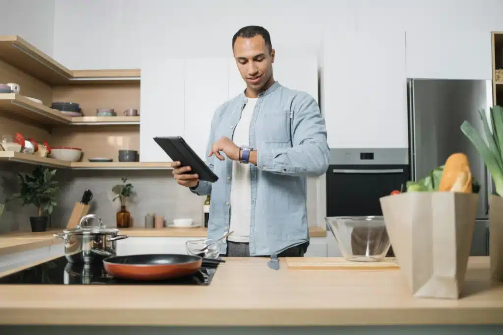 Cheerful middle aged indian man cooking salad for dinner at home, looking at watch