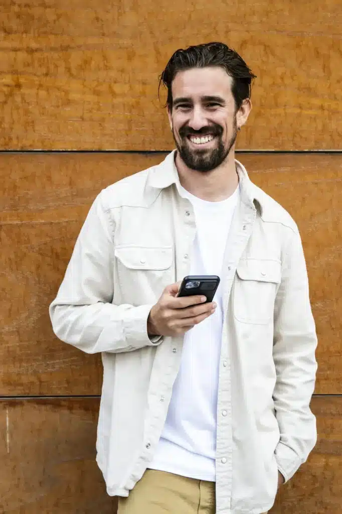 Confident handsome young guy texting with his phone and looking at camera. Happy and relaxed man