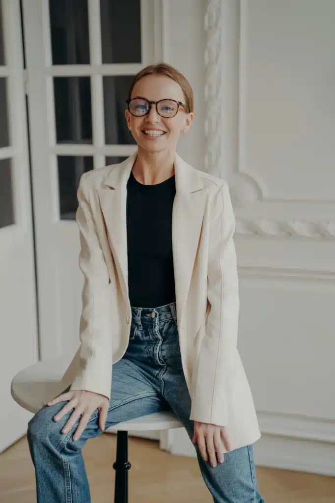 Confident woman sitting on table in apartment. Portrait of gorgeous smiling young adult lady.