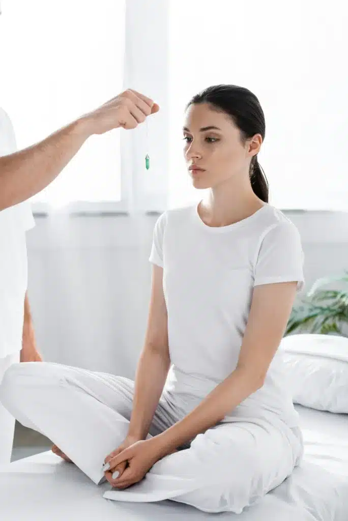 cropped view of hypnotist standing near woman and holding green stone near her face