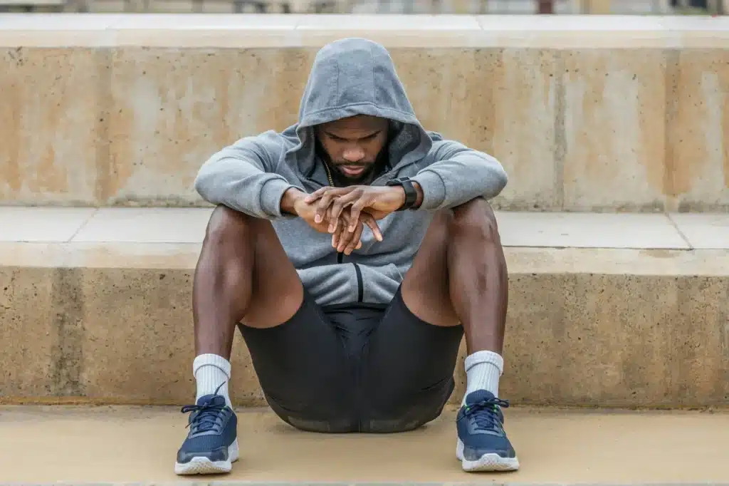 Depressed black sportsman sitting on ground