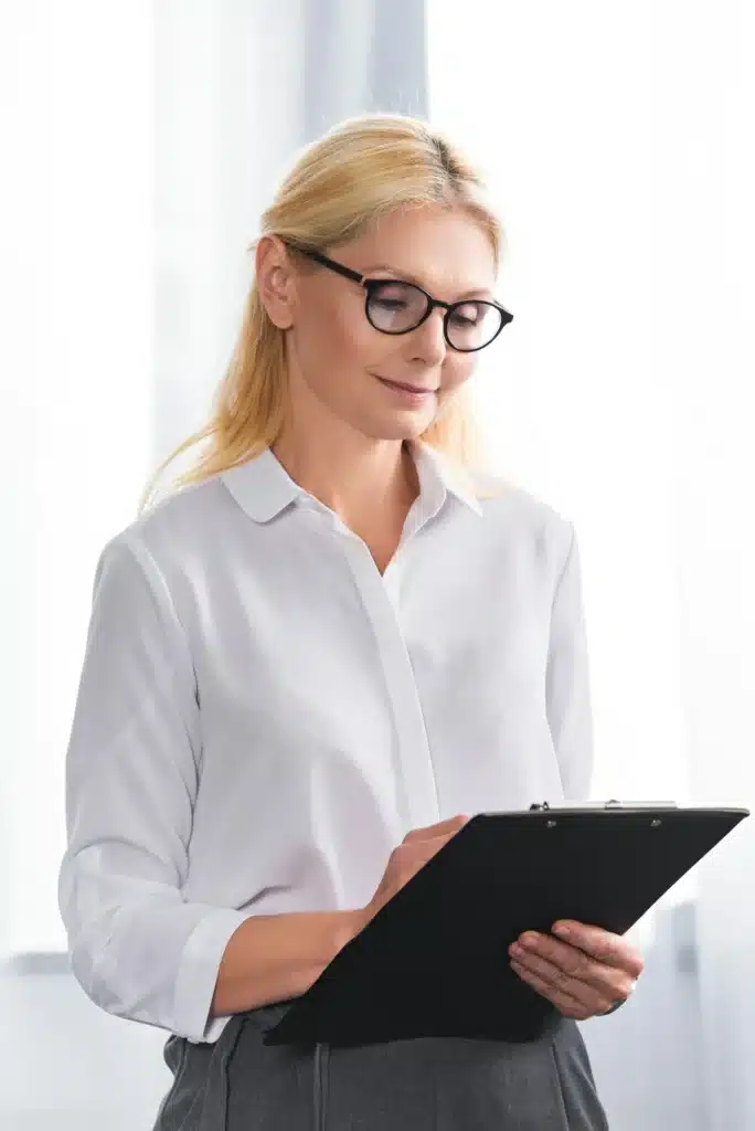 mature female therapist in eyeglasses writing in clipboard