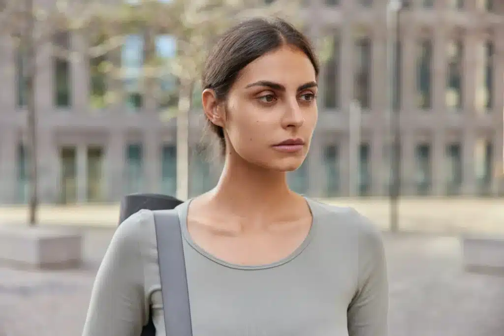 Pensive brunette woman focused into distance thinks how to improve health carries fitness mat dresse