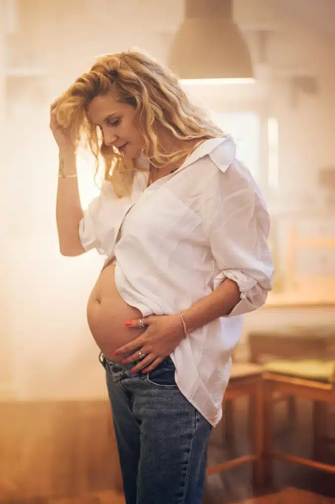 Portrait of pregnant woman standing at home holding hands on her belly