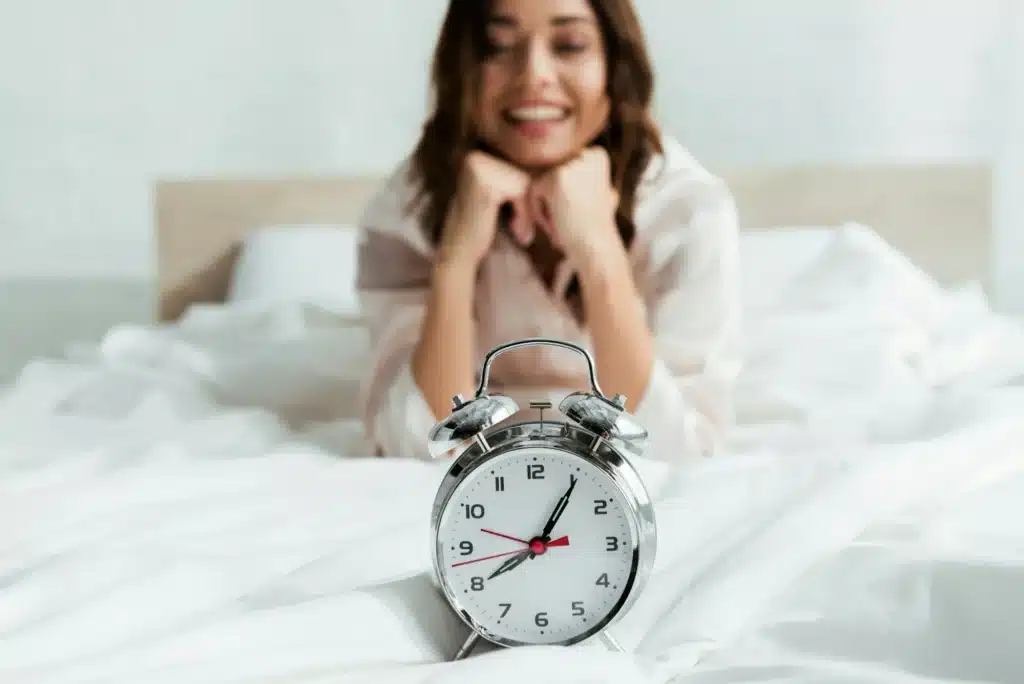 selective focus of attractive woman looking at alarm clock at morning