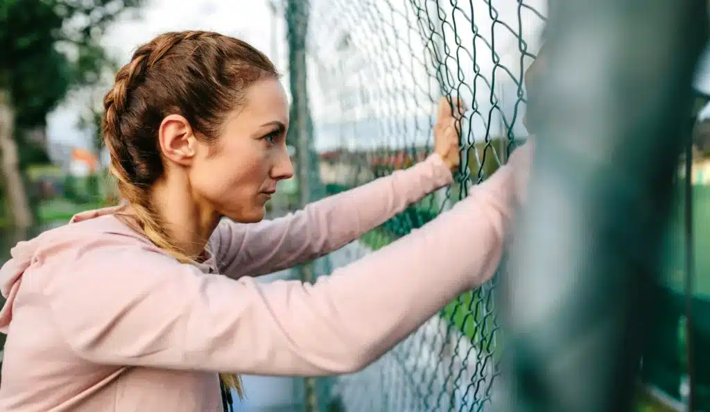 Serious portswoman with boxer braids leaning on a metal fence