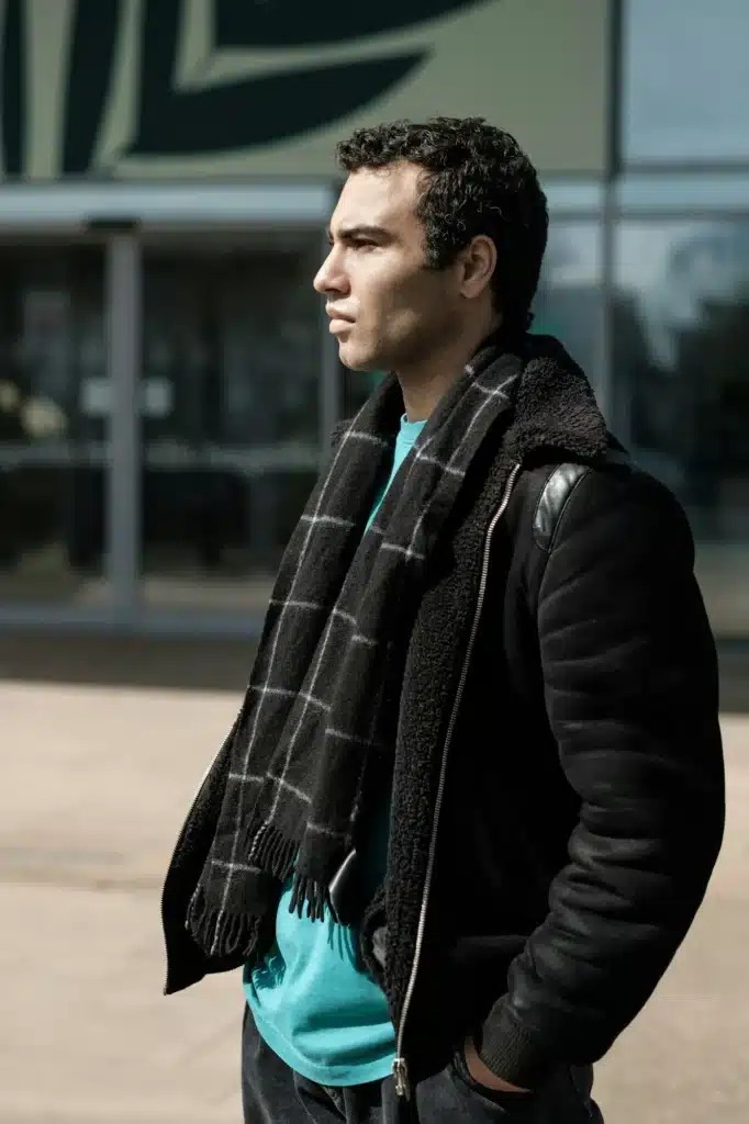 Serious young man wearing a black jacket is looking away in an urban environment.