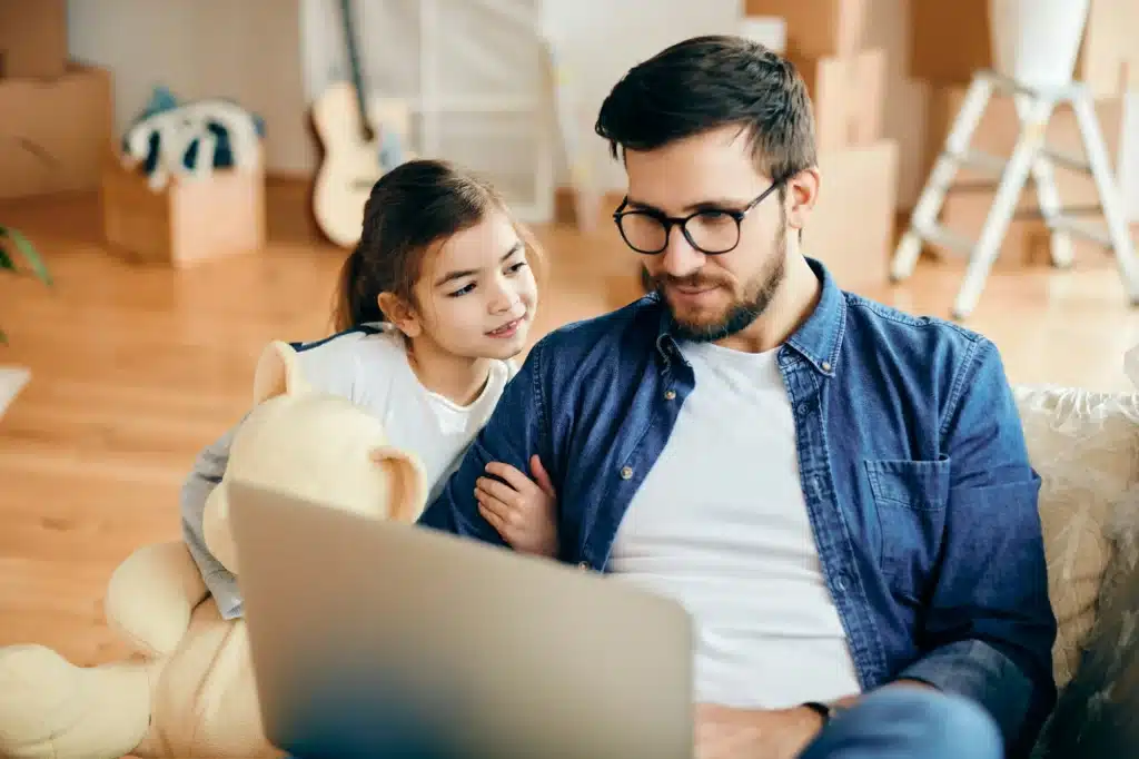 Smiling father and daughter using laptop at their new home.