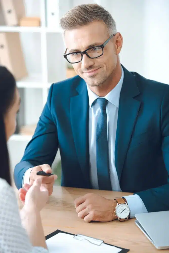 smiling insurance agent giving pen to female client at tabletop in office