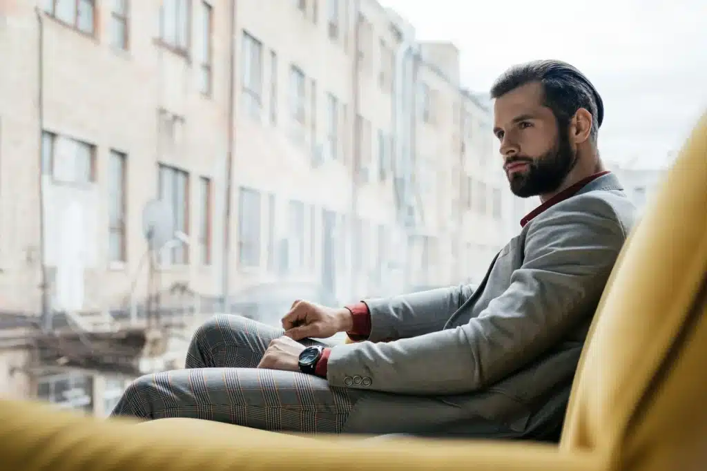 stylish pensive man sitting on yellow sofa at window