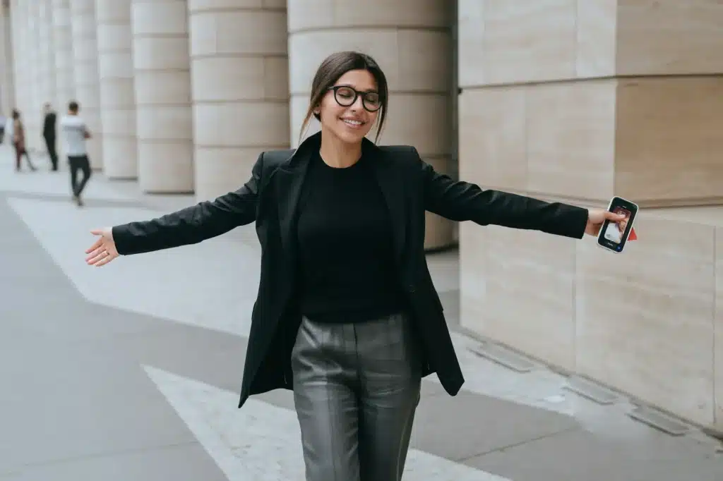 Successful young businesswoman in black jacket walking smiles eyes closed spreading hands feels free