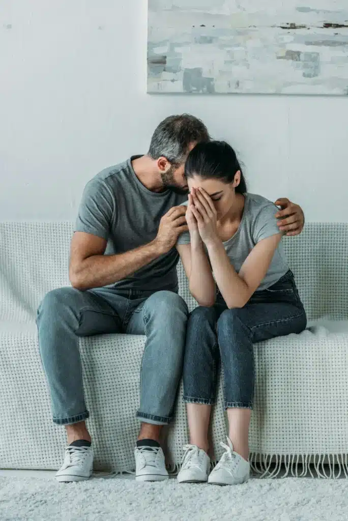 upset young man supporting depressed girlfriend while sitting together on couch