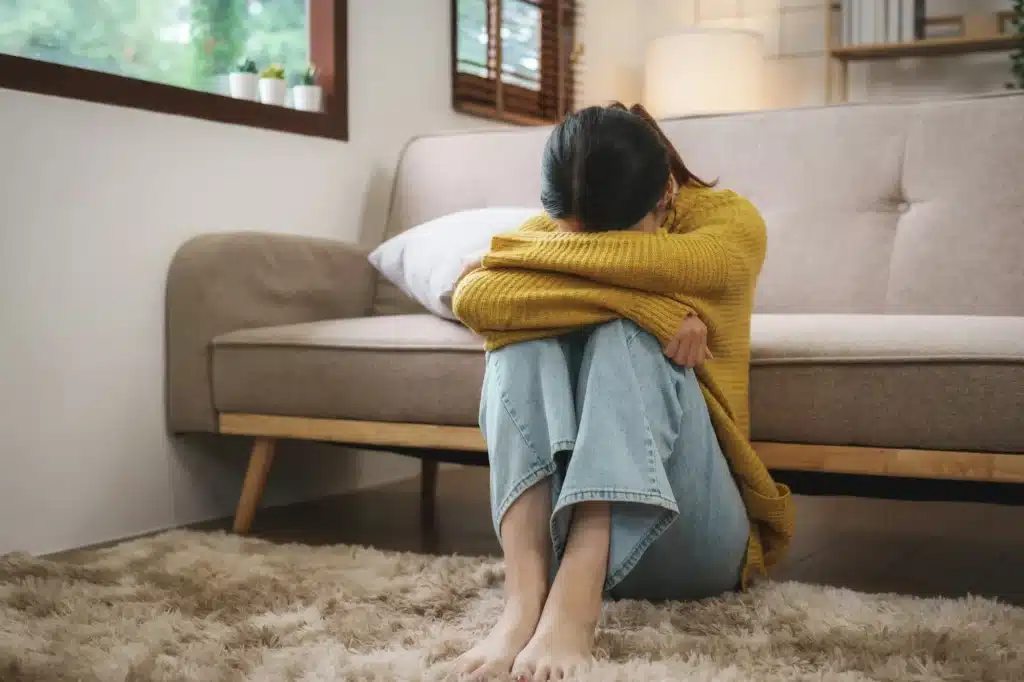 Young Asian woman suffering from work stress sits alone on the sofa at home discouraged. Desperate A