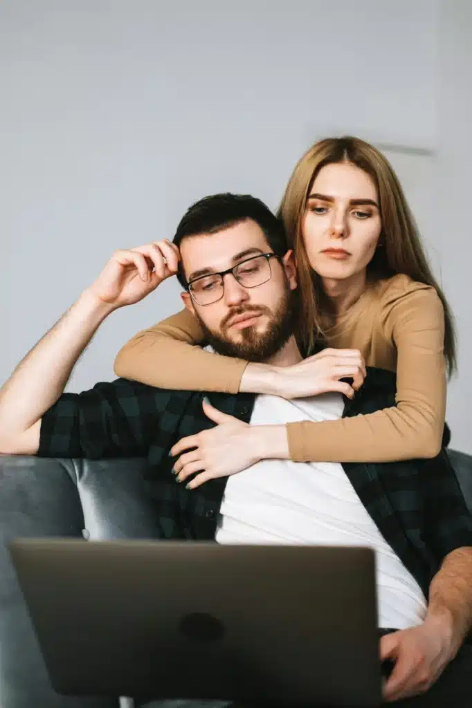 Young pensive couple using laptop computer and resting on the sofa at home together.