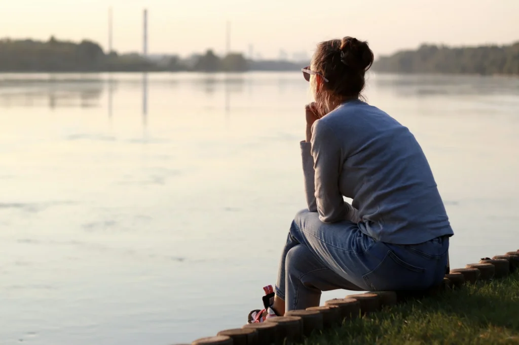 Young woman is sitting by the river bank and thinking. Sitting alone, deep thinking.