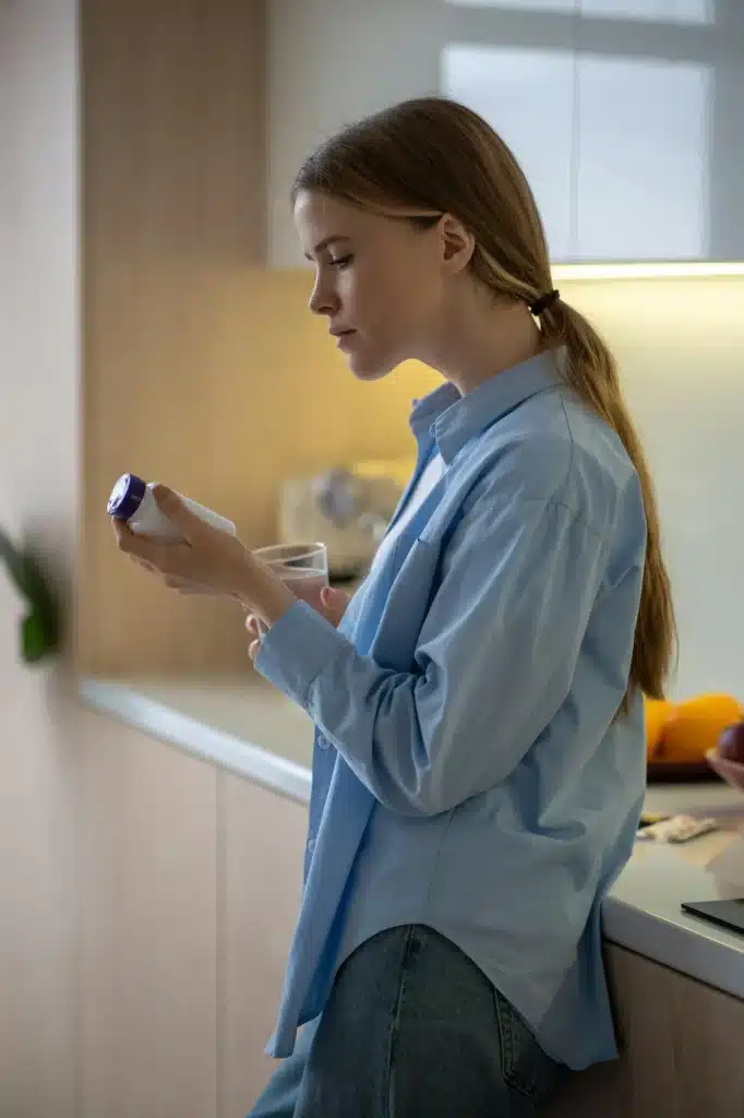 Focused woman with glass of water reading instruction of medication before taking on kitchen at home