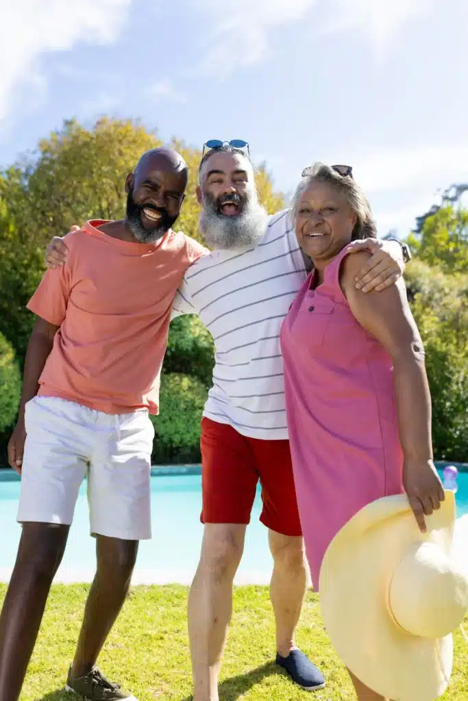 Group of senior friends smiling and embracing outdoors by pool on sunny day