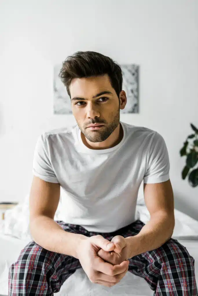 serious man in pajamas sitting on bed at home