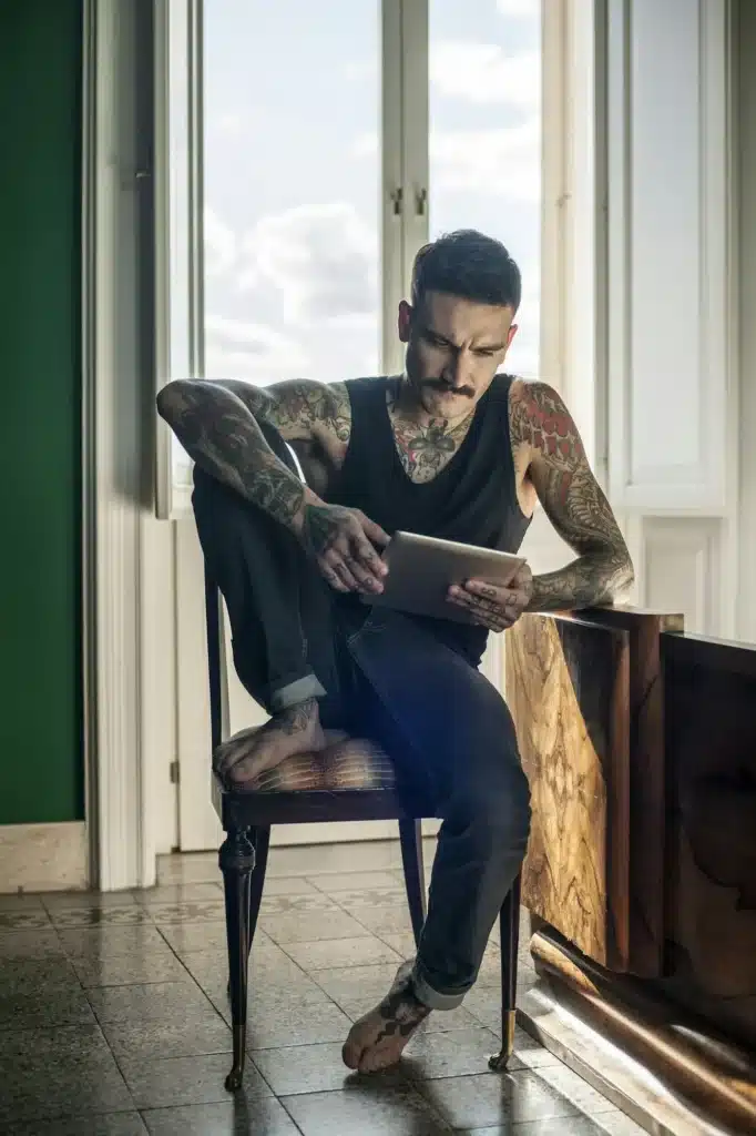 Man immersed in reading on his tablet by the window light.