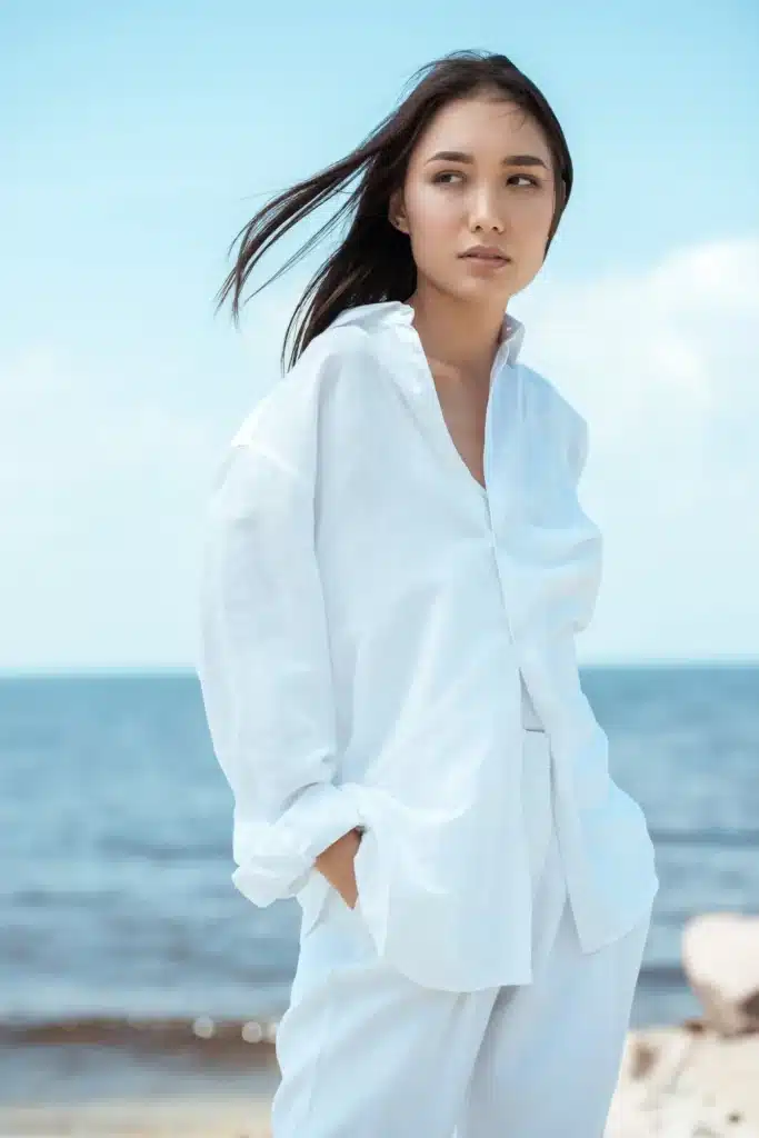 attractive young asian woman with hands in pockets looking away on beach