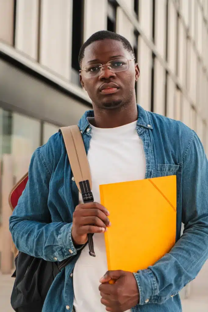 Vertical Serious African American student looking pensive at the camera, holding a folder and